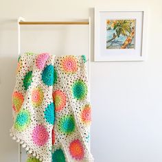 a colorful crocheted blanket hanging on a clothes rack next to a framed photograph