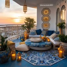 an outdoor living area with blue and white furniture on the balcony overlooking the ocean at sunset