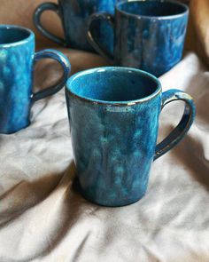 three blue coffee mugs sitting on top of a white cloth covered tablecloth,