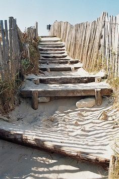 steps leading to the beach with sand and grass on either side that lead up to the fence