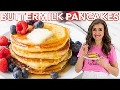 a woman standing in front of a stack of pancakes with berries and butter on top