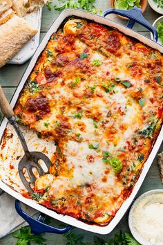 a casserole dish with meat and vegetables in it on a wooden table next to bread