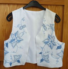 a white shirt with blue flowers on it hanging from a wooden hanger in front of a door