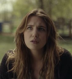 a woman with long hair and blue eyes looks at the camera while sitting in a park