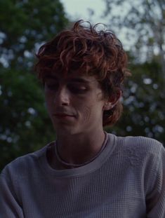 a young man with red hair is looking at his cell phone while standing in front of some trees