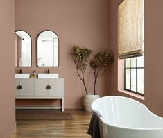 a bathroom with pink walls and wooden floors, two oval mirrors on the wall above the bathtub