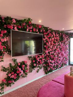 a tv mounted to the side of a wall covered in pink flowers and greenery