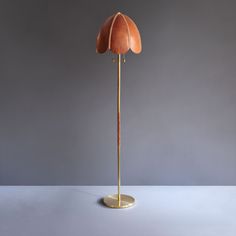 a gold floor lamp with an orange flower on it's base and a grey background