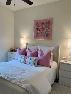 a white bed with pink and blue pillows in a bedroom next to two nightstands