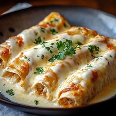 two enchiladas with cheese and parsley in a black plate on a table