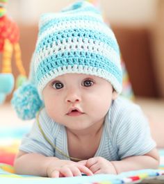 a baby laying on its stomach wearing a blue crocheted hat with pom poms