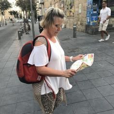 a woman walking down the street with a backpack on her back, looking at a map