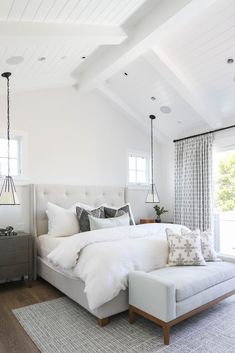 a bedroom with white bedding and pillows on top of the bedspread in front of two windows