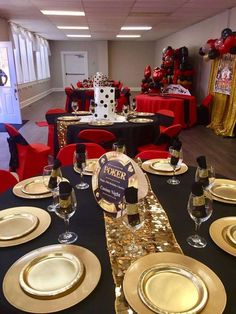 a table set up for a party with black and gold plates, silverware, and red chairs