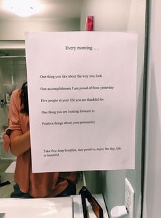 a woman holding a sign in front of her face while sitting on a bathroom sink