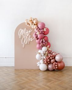 a balloon arch with pink, white and gold balloons on it in front of a wall