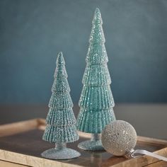 two glass christmas trees sitting on top of a wooden tray next to a silver ornament