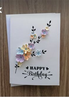 a happy birthday card with flowers and leaves on the front, sitting on top of a wooden table