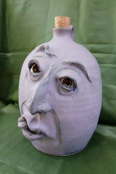 a white vase with a face painted on it's side and a cork top