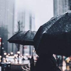 a person holding an umbrella in the rain on a city street with buildings and cars