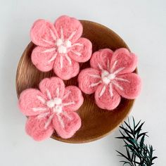 three pink crocheted flowers sitting on top of a wooden plate next to a plant