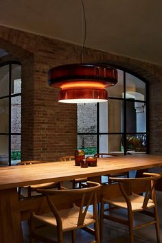 a wooden table with chairs and a light hanging from it's ceiling in front of large windows