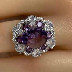 Details: Materials: Amethyst Gemstone, White Zircons, S925 Sterling Silver Plated with 18K White Gold Shape: Oval Size: Adjustable and fitable for all Descriptions: This oval shape design ring has one 12x10mm and six 3.5x3.5mm amethysts. The ring is made out of S925 sterling silver plated with 18K white gold. Surrounding the amethysts are twenty-four (24) white zircons, which make the amethysts stand out and shine. The arrangement of the amethysts makes it look like a flower shape from a distanc Luxury Cubic Zirconia Amethyst Ring Gift, Gemstone Accents Cluster Ring Gift, Round Multi-stone Amethyst Ring, Cluster Amethyst Ring As A Gift, Cluster Amethyst Ring Gift, Elegant Cluster Amethyst Ring For Anniversary, Elegant Amethyst Cluster Ring For Anniversary, Gift Cluster Amethyst Ring, Cluster Gemstones With Accent Stones As Gift