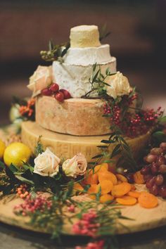 a three tiered cake sitting on top of a wooden plate covered in fruit and flowers