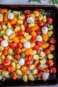 roasted tomatoes and mozzarella in a baking pan with basil leaves on the side