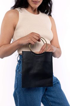 The Mini O Ring bag was inspired by our love of clean, minimalist design. The square and circle (and triangle are) the most reduced and basic geometric forms of any design language. The metal handles are sewn into the leather of the body so as to give the effect of the circle interrupting the square. This bag is just big enough to fit a phone, keys, and lip balm. This artisanal product is made of genuine leather. All scars are characteristics of the skin and not imperfections. We hope you enjoy Minimalist Bag With Round Handle For Everyday Use, Gold Rectangular Minimalist Bag, Minimalist Gold Rectangular Bag, Modern Everyday Tote Bag, Minimalist Bags With Gold-tone Hardware For Daily Use, Minimalist Rectangular Bags With Handle Drop, Gold Minimalist Rectangular Bag, Modern Square Bags With Metal Hardware, Chic Geometric Bag For Everyday Use