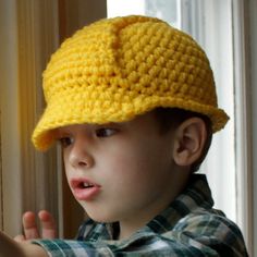 a young boy wearing a yellow crocheted hat and pointing at something in front of him