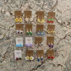 twelve pairs of earrings are displayed on a marble counter top, with cards attached to them