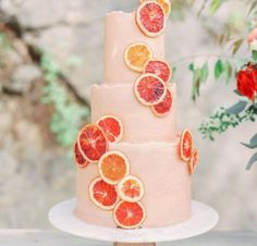 a three tiered cake with orange slices on top and flowers in the back ground