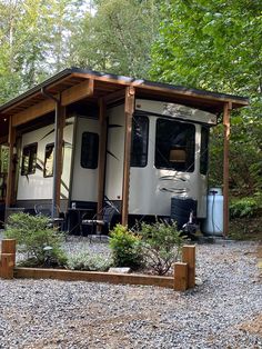 an rv parked in the woods next to a picnic table and grill area with chairs