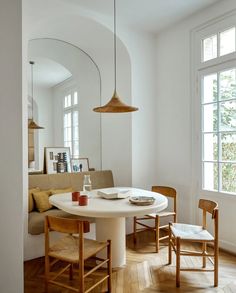 a white table and chairs in a room with wood flooring, arched doorways and windows