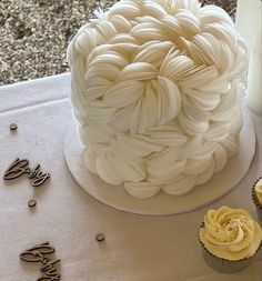 cupcakes are sitting on a table next to a white frosted cake with icing swirls