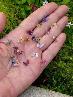 a person's hand is full of tiny butterflies on the grass and flowers in the background