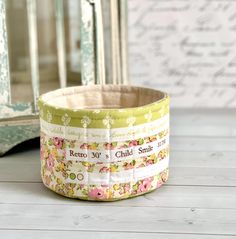 a close up of a bowl on a wooden floor near a mirror and wallpaper