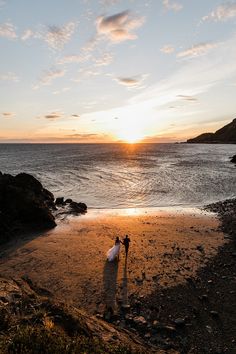 two people standing on the beach at sunset