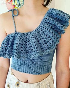 a woman wearing a blue crochet top with ruffles on the shoulders