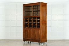 an old wooden cabinet with glass doors and wheels on the bottom shelf, in front of a white wall