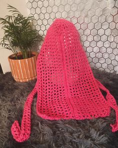 a pink crocheted bag sitting on top of a rug next to a potted plant