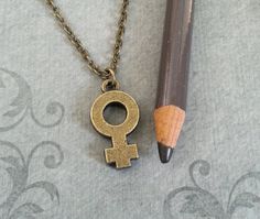 a pencil is laying next to a necklace with an old - fashioned female symbol on it