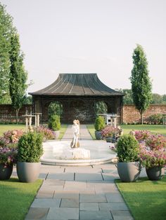 a dog sitting on top of a fountain surrounded by potted plants and flowers in front of a gazebo