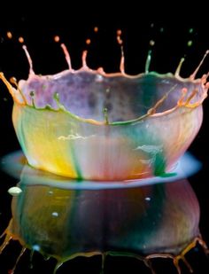 a colorful glass bowl sitting on top of a reflective surface with water droplets coming out of it