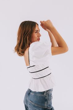 Add a touch of whimsy with our EXCLUSIVE Sunlit Veranda Top! This off white crop top boasts black accents and a cute black bow in front. Short, puff sleeves and a silver zipper in the back add charm, while elastic in the bodice allows for a comfortable and stretchy fit. Perfect for any occasion with its playful and flattering square neckline. Details Off white top with black accents Cropped fit Short, puff sleeves Black bow in front Silver zipper in back Elastic in bodice allowing for stretch Sq White Fitted Chic Crop Top, White Fitted Crop Top For Day Out, White Fitted Crop Top, Chic White Short Sleeve Crop Top, White Cropped Chic Top, White Fitted Summer Top, White Crop Top For Brunch, Trendy White Top For Brunch, Trendy White Tops For Brunch