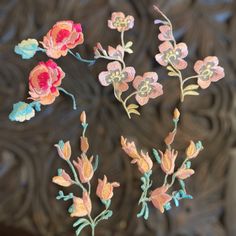 four embroidered flowers on a wooden surface with an intricate design in the backround