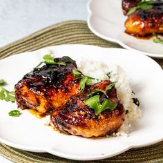 two white plates topped with meat covered in sauce and garnished with green leaves