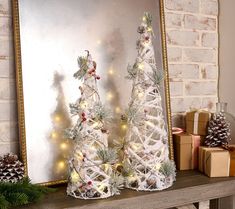 two white christmas trees sitting on top of a mantle next to a mirror and presents