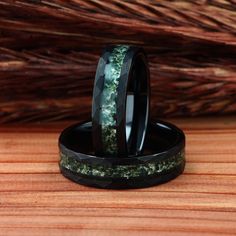 two wedding bands with green and black marble inlays on wooden table next to tree branches